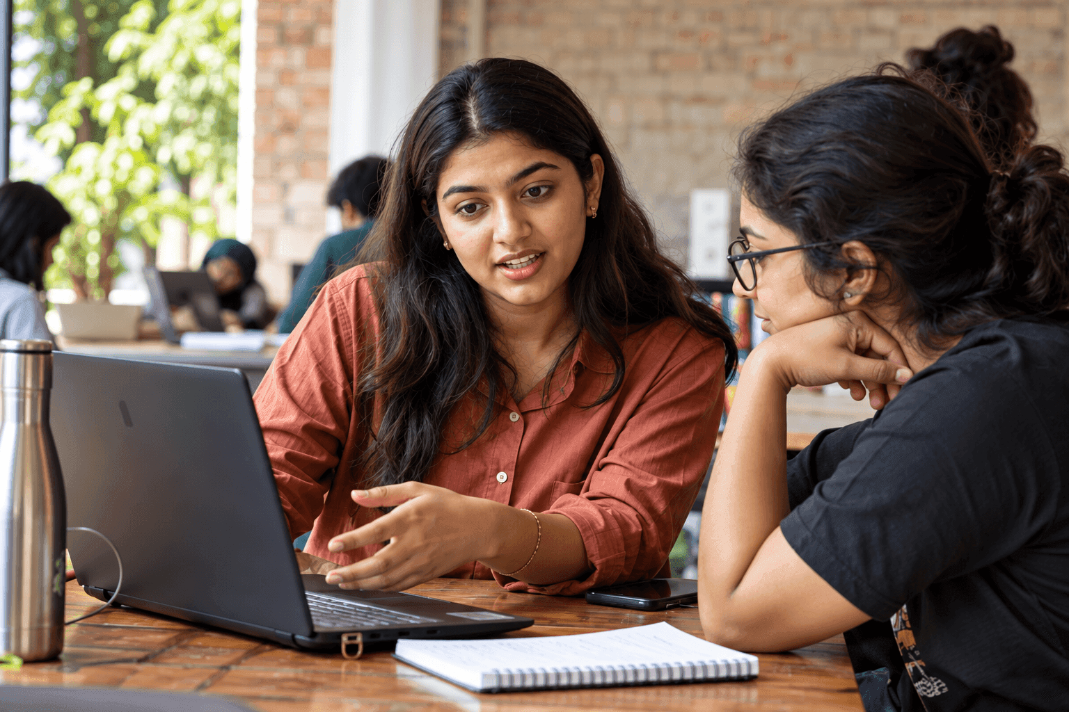 Student explaining her work to a classmate at a laptop